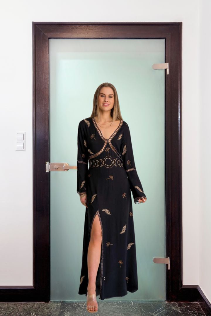 Woman in a black dress with gold patterns standing in front of a glass door.