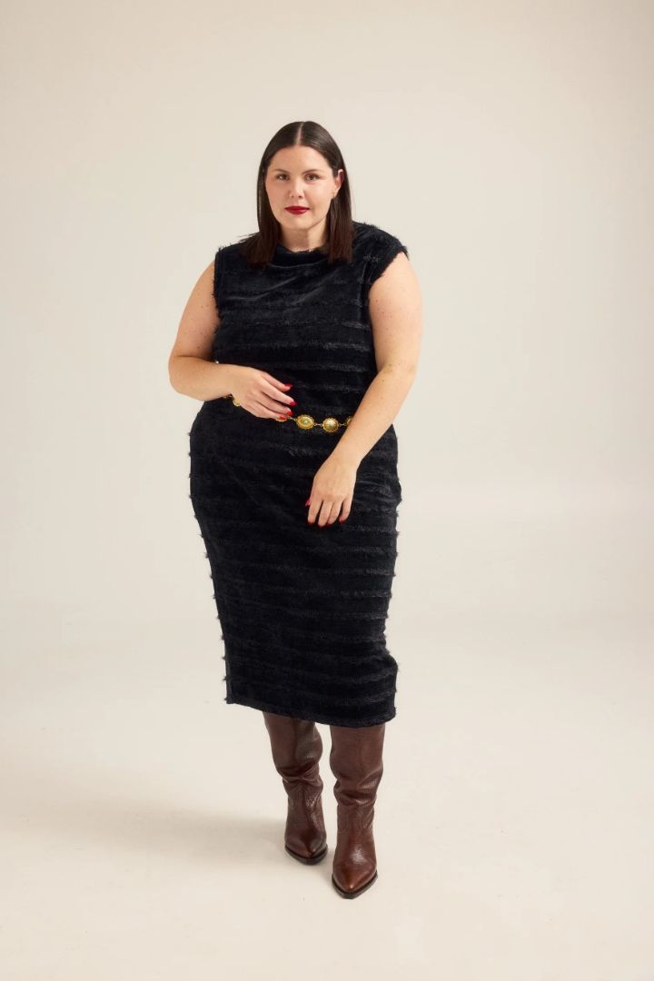 Woman wearing a black textured dress with brown boots on a beige background