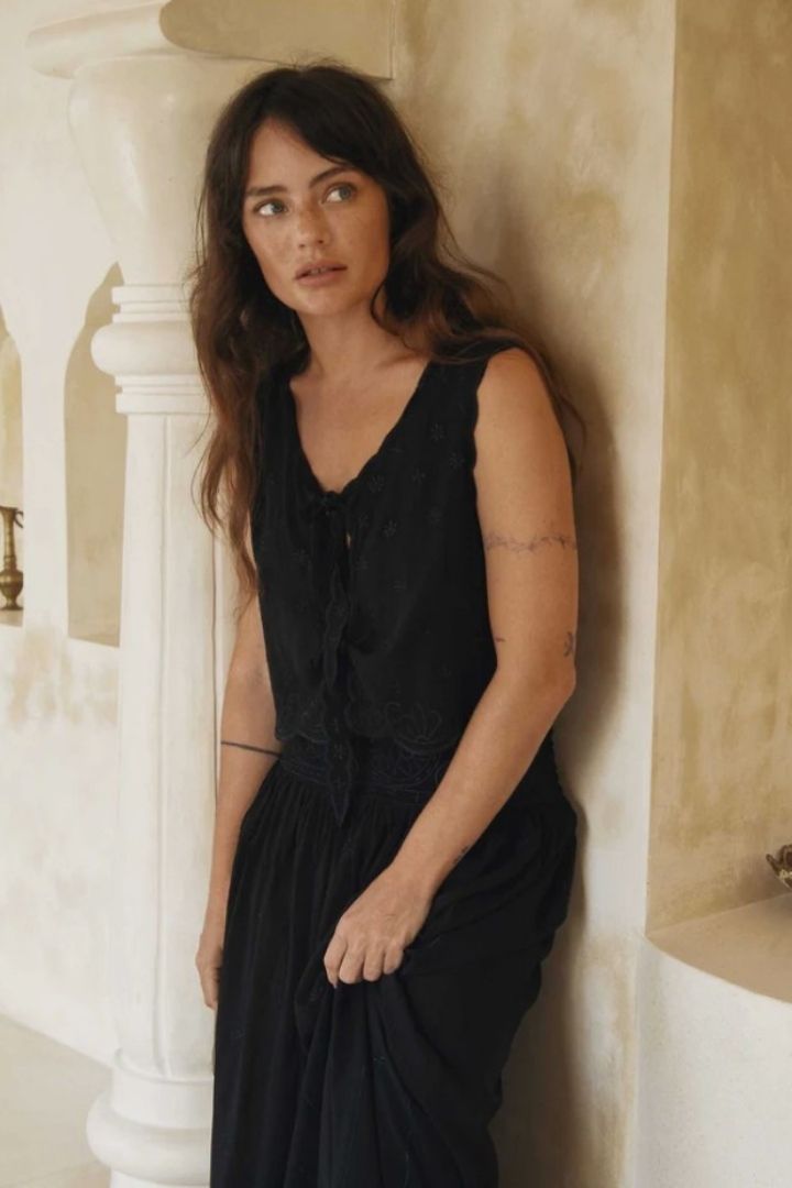 Woman in a black top and skirt standing against a light-colored wall.