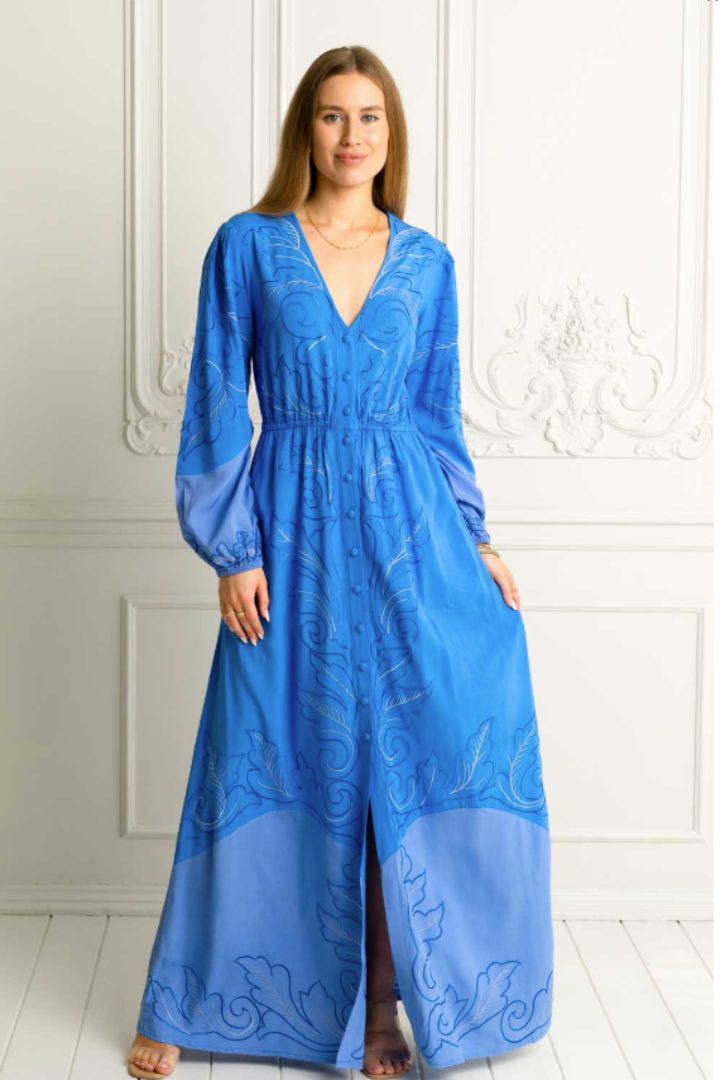 Woman wearing a blue embroidered long sleeve dress with buttons against a white wall