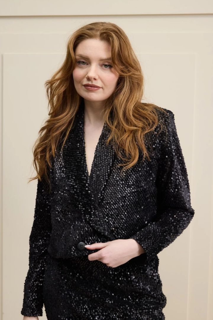 Woman wearing a black sequin blazer against a neutral background