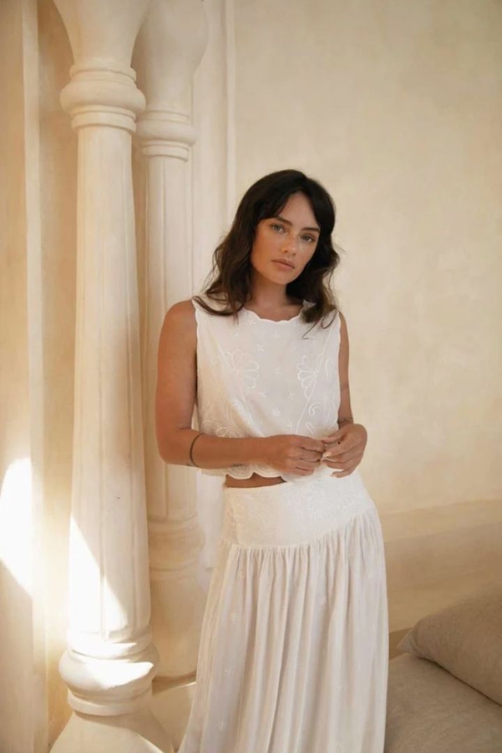 Woman in a white top and maxi skirt standing in a softly lit room with columns.