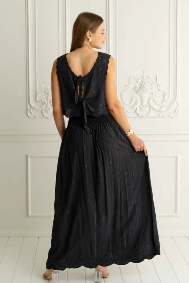 Woman wearing a black  top and skirt back view with a white wall background