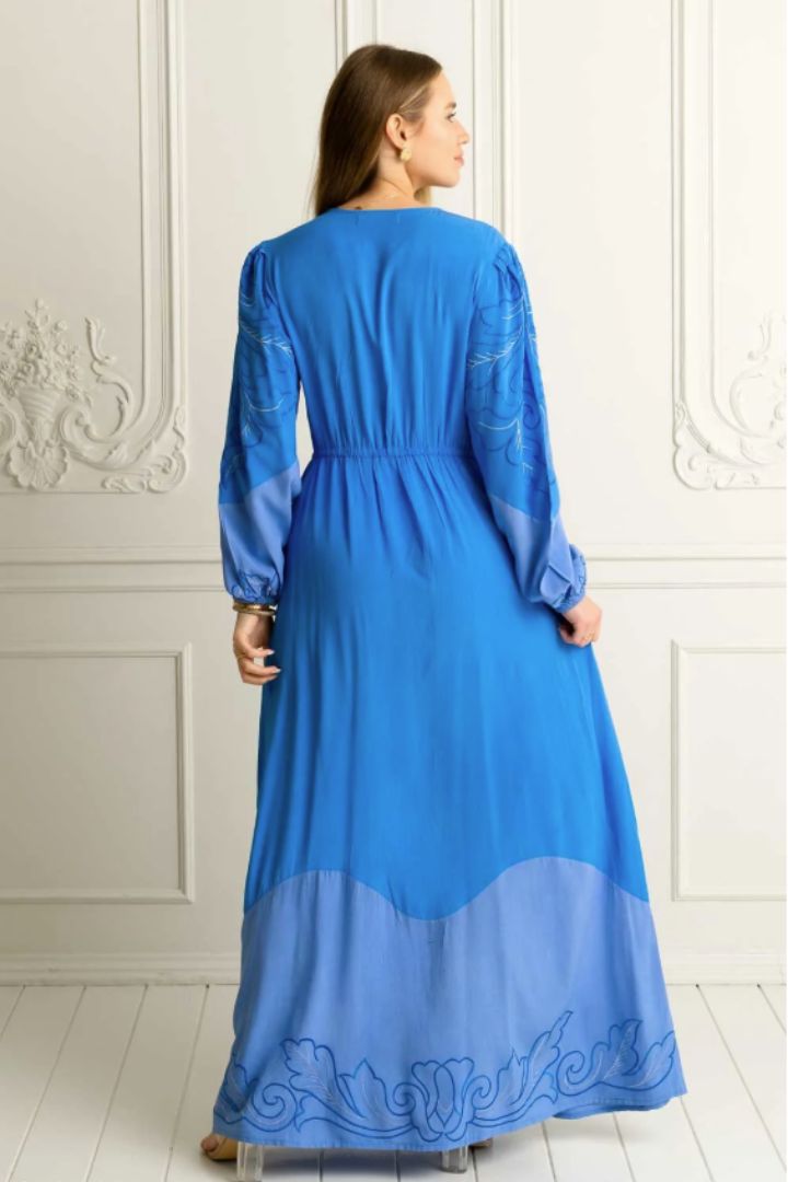 Woman wearing a blue embroidered long sleeve dress with buttons against a white wall with a back view of the dress
