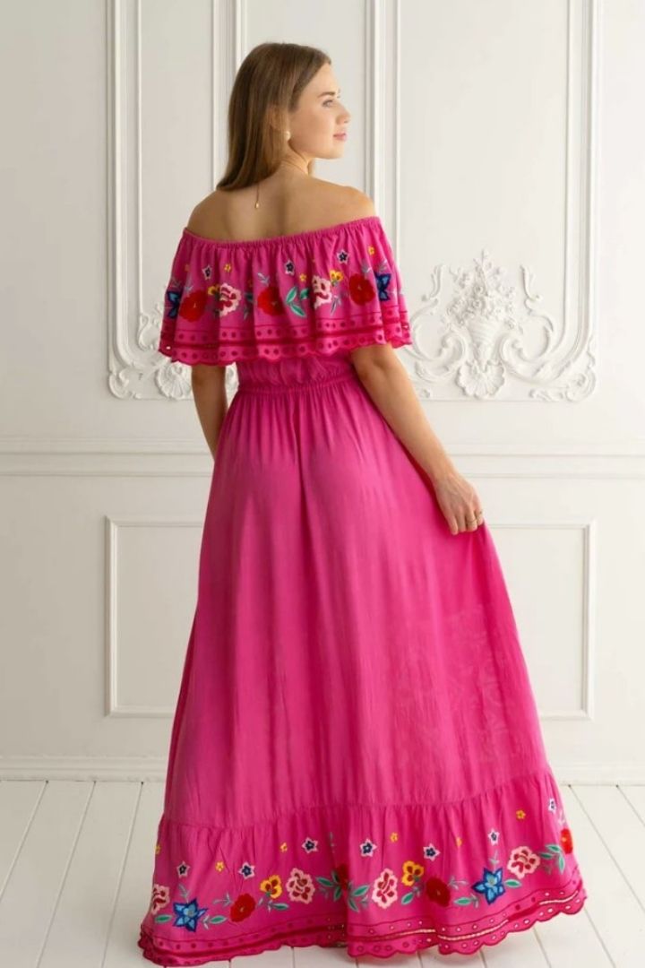 Back view of woman wearing a pink off-shoulder dress with floral embroidery against a white wall.