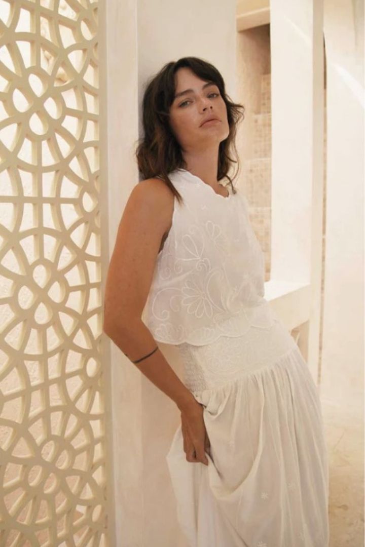 Woman in a white top and maxi skirt standing against a decorative wall.