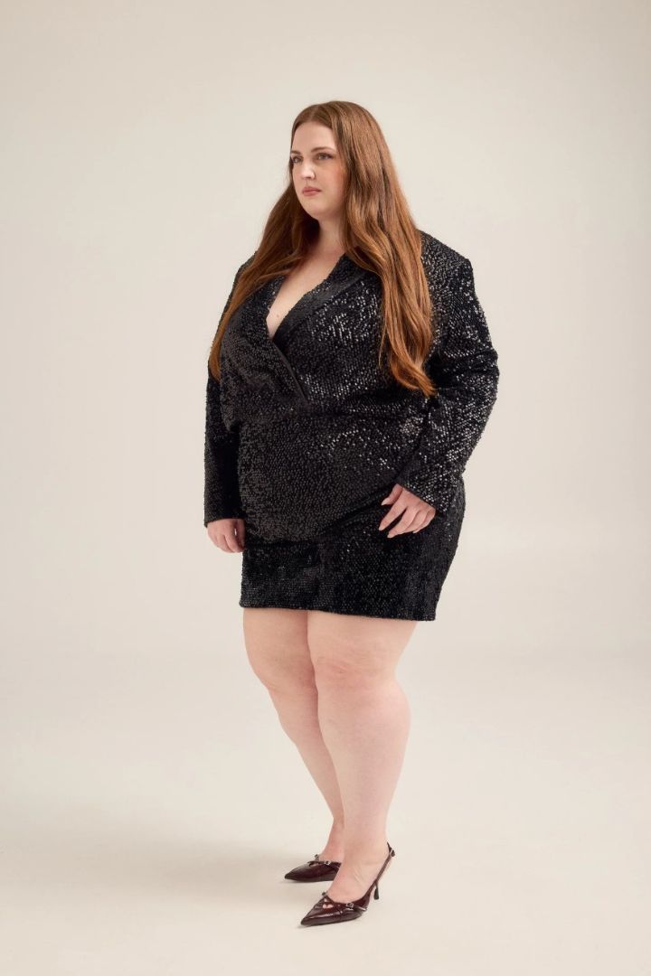 Woman wearing a black sequin blazer and skirt against a plain background