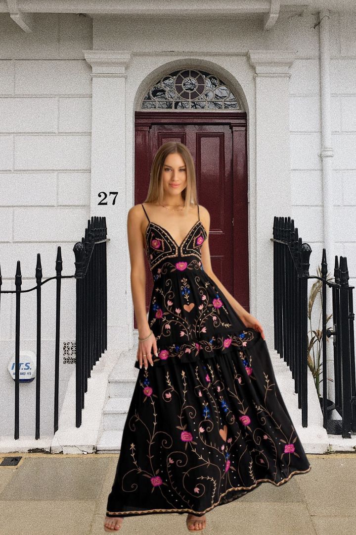 Woman in a black embroidered dress standing in front of a white building with a red door.