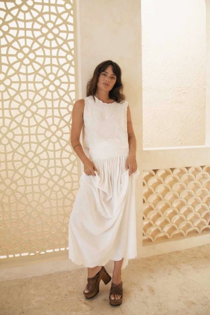 Woman wearing a white top and maxi skirt standing against a decorative wall.