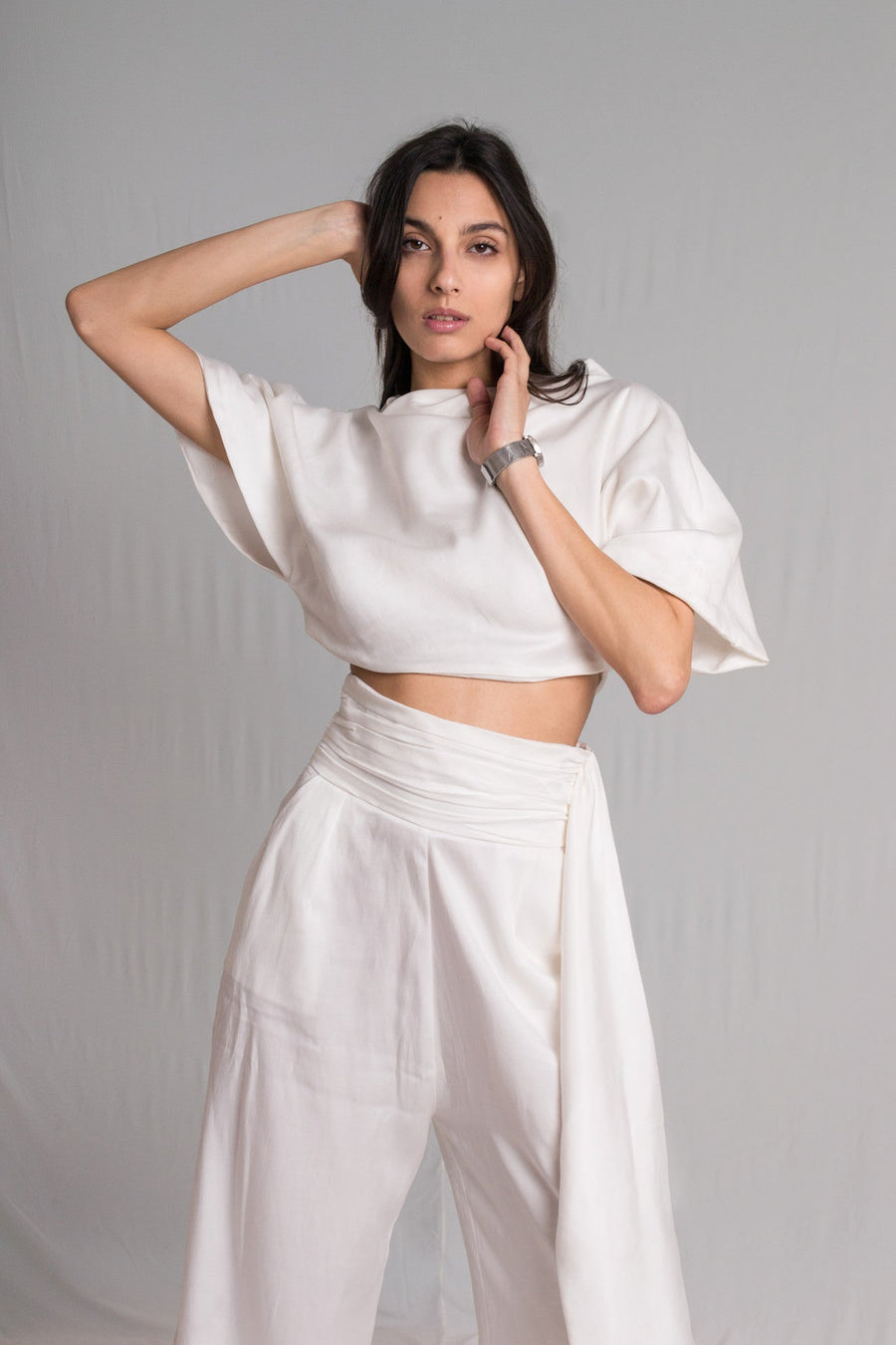 White cropped top with a relaxed cowl neckline and high-waist pants with a hidden zipper pockets and a hand-ruched waistband